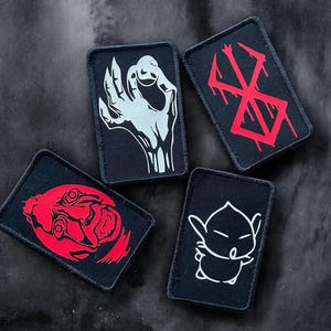 Peut inclure: Cinq patchs en tissu noir avec des motifs graphiques blancs et rouges. Les patchs représentent une main, un symbole, un visage, une créature et un symbole.