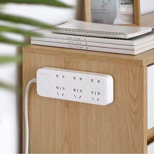 May include: White power strip with six sockets mounted on a wooden surface. The power strip has a white cord and a small white button on the side.