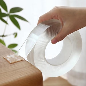 Könnte beinhalten: Eine Rolle durchsichtiges, transparentes Klebeband. Das Band wird von einem Spender abgewickelt und in einer Hand gehalten.