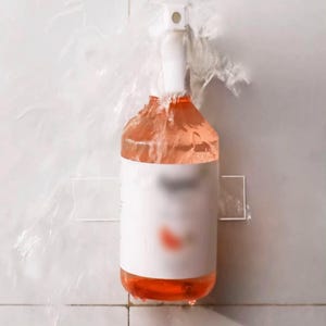 May include: A clear spray bottle with a white label and a pink liquid inside. The bottle is mounted on a white tiled wall with a clear adhesive strip.