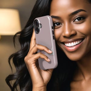 Puede incluir: Una funda de tel&eacute;fono de color malva claro con una c&aacute;mara de doble lente y botones laterales. La funda se sostiene en una mano con cabello largo y oscuro en el fondo. La funda del tel&eacute;fono es de color s&oacute;lido con un acabado liso.