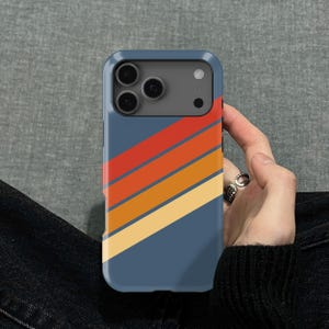 Pu&ograve; includere: Custodia per telefono blu con un design retr&ograve;. La custodia presenta strisce diagonali rosse, arancioni e gialle. La custodia del telefono &egrave; tenuta in mano da una persona.