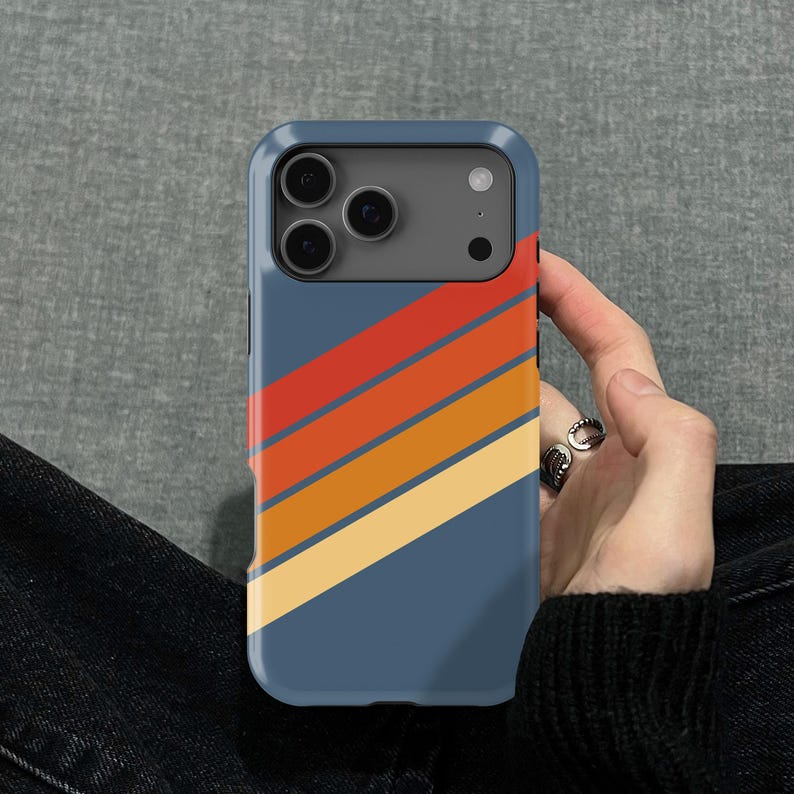 Pu&ograve; includere: Custodia per telefono blu con un design retr&ograve;. La custodia presenta strisce diagonali rosse, arancioni e gialle. La custodia del telefono &egrave; tenuta in mano da una persona.