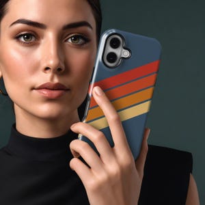 Pu&ograve; includere: Una custodia per telefono blu navy con un design retr&ograve; con strisce orizzontali rosse, arancioni e gialle. La custodia &egrave; tenuta da una persona. La custodia del telefono ha un ritaglio per la fotocamera.