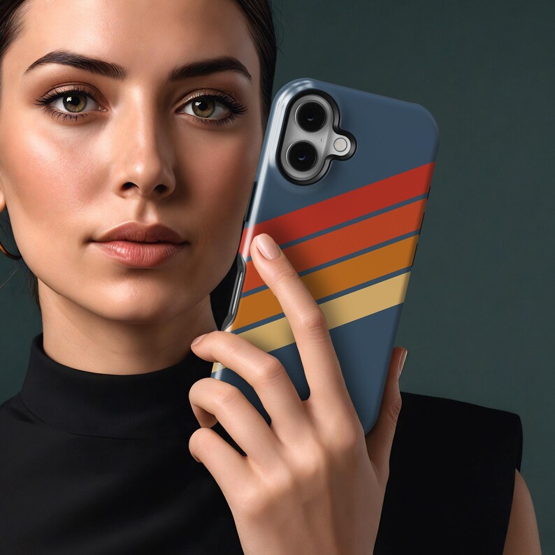 Pu&ograve; includere: Una custodia per telefono blu navy con un design retr&ograve; con strisce orizzontali rosse, arancioni e gialle. La custodia &egrave; tenuta da una persona. La custodia del telefono ha un ritaglio per la fotocamera.