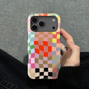 May include: A phone case featuring a vibrant checkerboard design in pink, orange, yellow, green, and blue. The case has a camera aperture and is held in a hand.