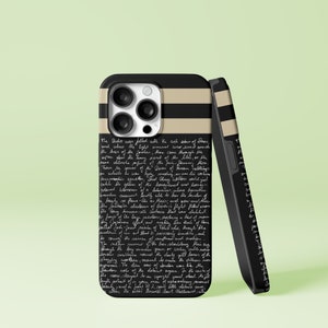 Op de afbeelding: Zwarte iPhone-hoes met een beige en zwart gestreept ontwerp. De hoes heeft handgeschreven tekst in het wit. De telefoonhoes leunt tegen een andere hoes met hetzelfde ontwerp. De hoesjes staan op een lichtgroene achtergrond.