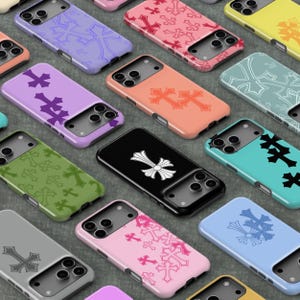 May include: A collection of smartphone cases in various colors including lavender, peach, black, pink, and light blue, each featuring a repeating or singular cross emblem pattern and a cutout for a triple-lens camera system on the back.