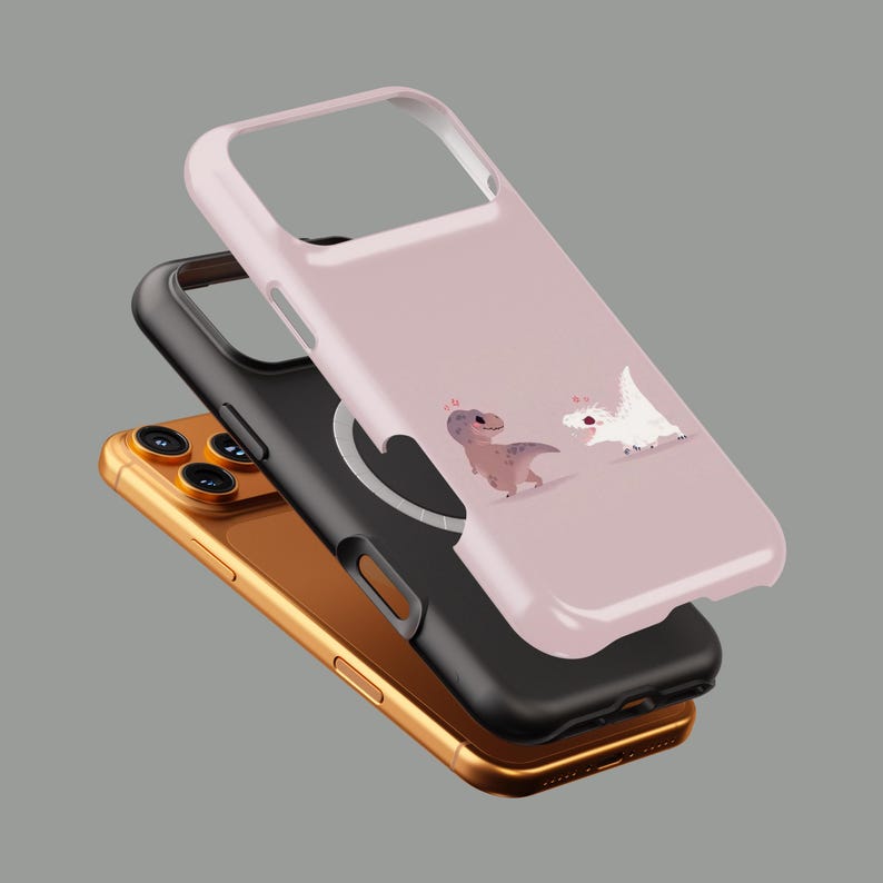 Puede incluir: Un smartphone dorado con una funda negra y una funda rosa claro. La funda rosa claro presenta una ilustraci&oacute;n de dibujos animados de dos dinosaurios. Las fundas est&aacute;n dise&ntilde;adas para proteger el tel&eacute;fono.