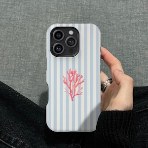 Może przedstawiać: Etui na telefon z jasnoniebiesko-białym wzorem w paski i koralowym wzorem rafy koralowej. Etui ma błyszczące wykończenie. Etui jest trzymane przez osobę.