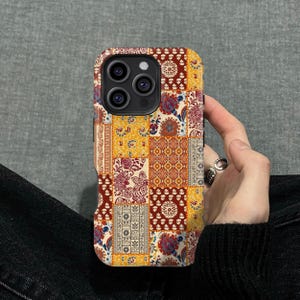 May include: A colorful phone case with a patchwork design. The case features a mix of patterns in shades of yellow, red, and brown. The design includes floral and geometric motifs, creating a unique and eye-catching accessory.