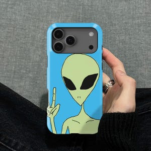 Puede incluir: Funda de teléfono azul claro con un diseño de alienígena de dibujos animados. El alienígena tiene una cabeza verde, ojos negros y hace un gesto con la mano. La funda tiene un parachoques protector azul.