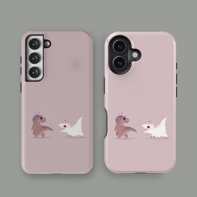 Puede incluir: Dos fundas para tel&eacute;fono de color rosa empolvado. Cada funda presenta una ilustraci&oacute;n de dibujos animados de un Tyrannosaurus Rex marr&oacute;n y un dinosaurio blanco. Las fundas est&aacute;n dise&ntilde;adas para diferentes modelos de tel&eacute;fono.