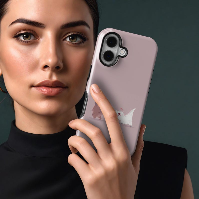 Puede incluir: Funda de tel&eacute;fono rosa claro con una ilustraci&oacute;n de dibujos animados de dos peque&ntilde;as criaturas parecidas a dinosaurios. Una es rosa y la otra blanca. La funda tiene un borde negro para la lente de la c&aacute;mara y la sostiene una persona.