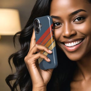 Pu&ograve; includere: Una custodia per smartphone blu navy con un design a strisce retr&ograve; in rosso, arancione, giallo e beige. La custodia ha un ritaglio per la fotocamera e dettagli dei pulsanti. La custodia del telefono &egrave; tenuta in una mano.
