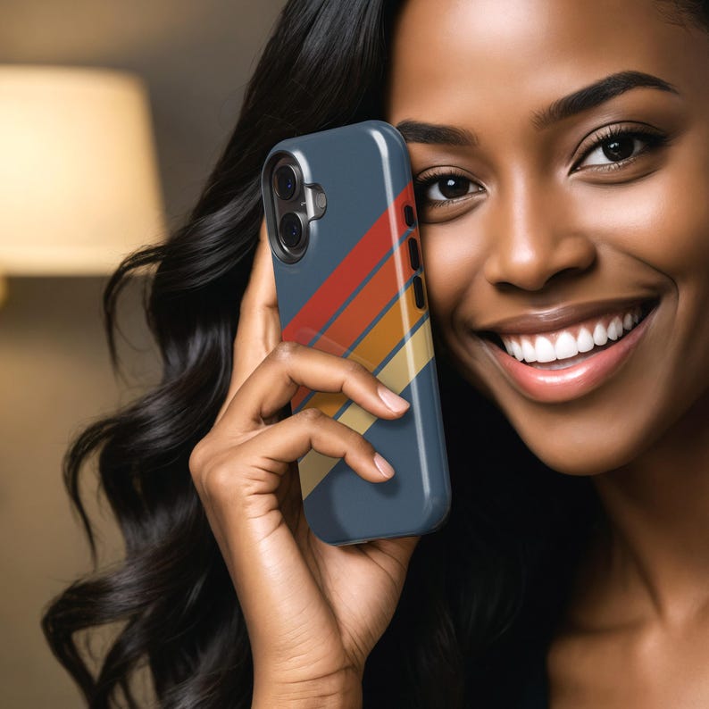 Pu&ograve; includere: Una custodia per smartphone blu navy con un design a strisce retr&ograve; in rosso, arancione, giallo e beige. La custodia ha un ritaglio per la fotocamera e dettagli dei pulsanti. La custodia del telefono &egrave; tenuta in una mano.
