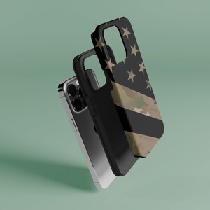 May include: A black phone case with a camouflage and American flag design. The case is shown with a black phone inside.