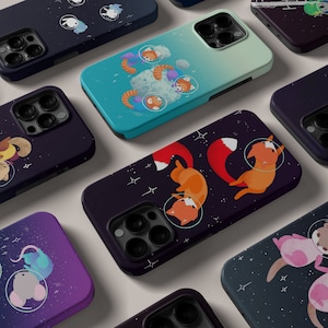 May include: A collection of phone cases featuring various animal illustrations in a space theme. The cases are black, blue, purple, and dark grey with white stars and planets. The animals include a red panda, a fox, a mouse, and a cat.