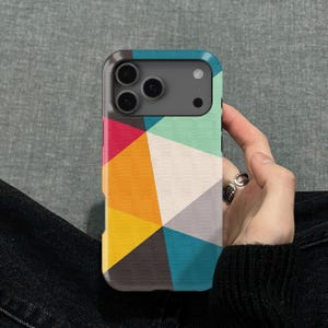 Könnte beinhalten: Handyhülle mit farbenfrohem geometrischem Muster. Das Design zeigt Dreiecke in Rot, Orange, Gelb, Türkis, Grau und Weiß. Die Hülle hat einen schwarzen Rand und einen Kameraausschnitt.