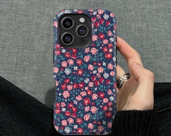 May include: A navy blue phone case with a floral pattern of pink and red flowers and green leaves. The case has a protective design with a camera cutout and is held in a hand.