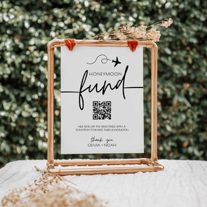 May include: White sign with black text that reads "Honeymoon fund" with a stylized airplane icon and a QR code. The sign is in a copper pipe frame.