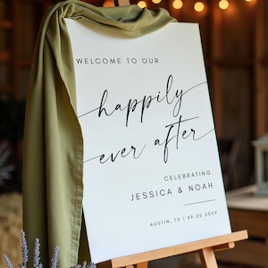 May include: A white sign on a wooden easel with the words "Welcome to our happily ever after" in black script. The sign celebrates Jessica & Noah in Austin, TX, on 09.20.20xx. A green cloth drapes over the top of the sign.