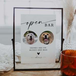 Puede incluir: Un letrero enmarcado con las palabras "open BAR" en escritura elegante. Debajo se presentan dos retratos de perros, con el texto "DRINKS ARE ON BUDDY AND MAX" y "cheers". El letrero está en un marco de cristal.
