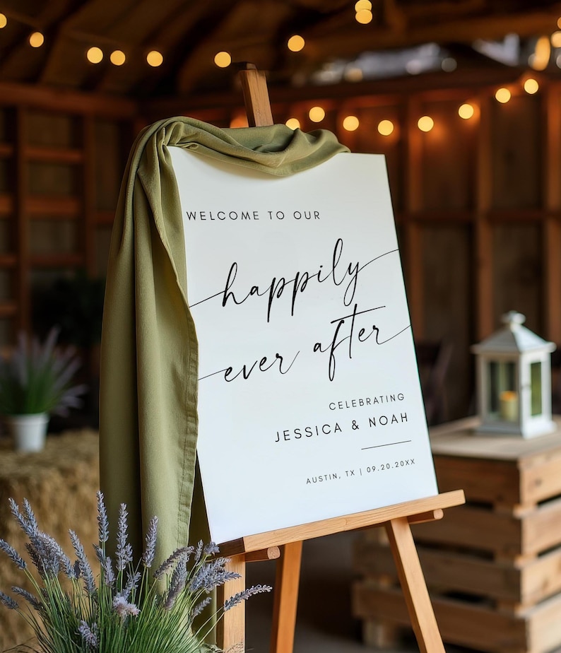 May include: A white sign on a wooden easel with the words "Welcome to our happily ever after" in black script. The sign celebrates Jessica & Noah in Austin, TX, on 09.20.20xx. A green cloth drapes over the top of the sign.