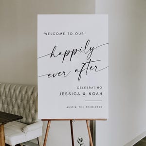 May include: A white wedding sign on a wooden easel. The sign reads "WELCOME TO OUR happily ever after CELEBRATING JESSICA & NOAH AUSTIN, TX | 09.20.20XX" in black script and block lettering. The sign is displayed indoors.