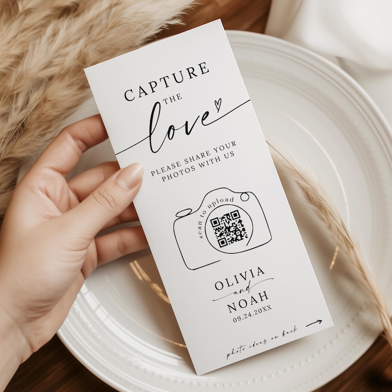 May include: A white wedding card held by a person. The card features the text "CAPTURE the love" in a script font, along with "PLEASE SHARE YOUR PHOTOS WITH US." A camera graphic with a QR code is also present, along with names and a date.