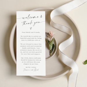 May include: A white card with black text that reads "welcome & thank you" with a small heart symbol. The text continues with a message to family and friends expressing gratitude for their presence at a celebration. The card is signed "With love, Jossien and Noah."