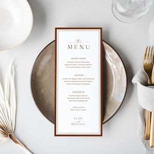 May include: A rectangular wedding menu card with a dark brown border and white center, featuring the text THE MENU, APPETIZERS, ENTREE, DESSERTS, and the names ELSIE and MICHAEL, centered on a round plate with gold cutlery and a grey napkin.