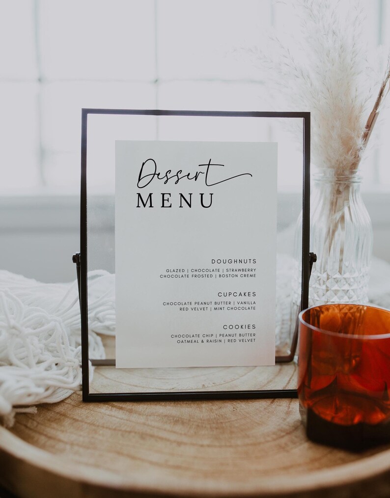 May include: A black framed menu with the word "Dessert Menu" written in cursive. The menu lists various dessert options, including doughnuts, cupcakes, and cookies.