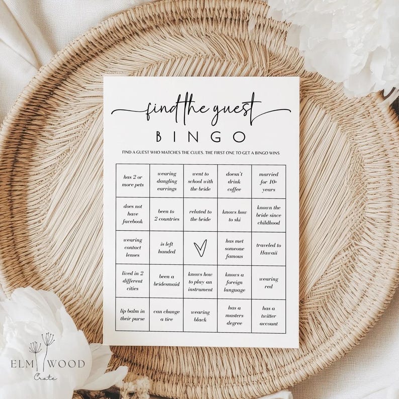 May include: A white "Find the Guest Bingo" game card with black text, featuring a grid of prompts. The card is on a woven tray. The game is designed to find guests who match the clues. The Elm Wood Crate logo is at the bottom.