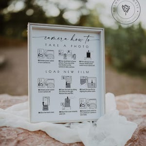 May include: A white framed sign with black text and illustrations explaining how to use an instant camera. The sign reads "camera how to take a photo" and "load new film".