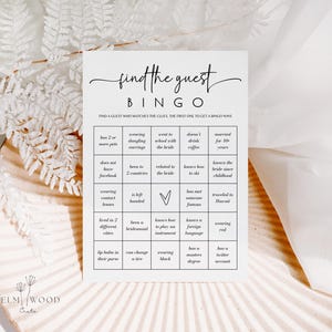 May include: A white Bingo game card with the text "find the guest" in elegant script. The card features a grid with various prompts like "wearing dangling earrings" and "knows how to ski". The card is designed for a wedding or bridal shower game.