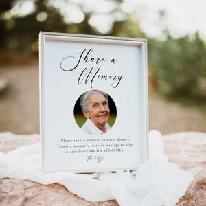 May include: A white rectangular sign in a light-colored frame featuring the text Share a Memory in black script, a circular photograph of an elderly person, and the text Please take a moment to write down a favorite memory, story or message to help us celebrate the life of [NAME]. Thank You.