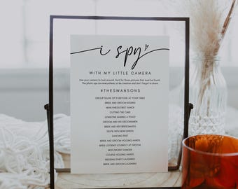 Può includere: Un cartello incorniciato in nero con sfondo bianco e il testo "i spy with my little camera" e "#theswansons". Il cartello elenca una varietà di idee per foto di matrimonio, come "la sposa e lo sposo che si baciano", "il taglio della torta" e "i piedi che ballano".