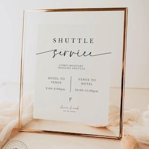 May include: A rectangular sign in a thin metallic gold frame featuring black text on a white background. The text reads SHUTTLE service, COMPLIMENTARY WEDDING SHUTTLE, HOTEL TO VENUE 2:00-3:00pm, VENUE TO HOTEL 10:00-11:00pm, and olivia & noah 09.24.20XX.