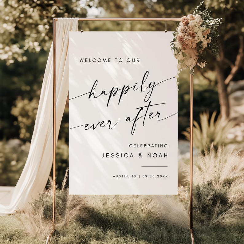 May include: A white wedding sign with the words "Welcome to Our Happily Ever After" in elegant black script. The sign also includes the names Jessica & Noah, and the location and date. The sign is on a gold metal stand, decorated with flowers.