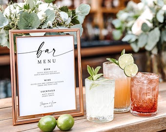 May include: A rose gold framed bar menu with the word "bar" in elegant script. The menu lists beer, wine, and cocktails. Three cocktails with lime and mint garnishes sit next to the menu. Two limes are in the foreground.