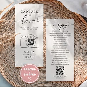May include: Two rectangular wedding signs with text and illustrations. One sign says "Capture the love" with a camera graphic and QR code. The other sign says "i spy" with a list of photo prompts and a QR code. Both signs include the names Olivia and Noah and a date.