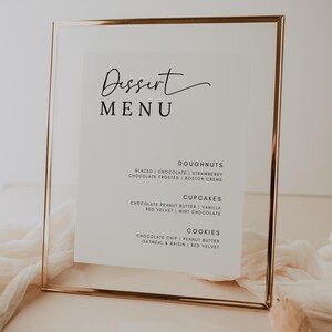 May include: A gold-framed menu board with a white background and black text. The menu lists dessert options, including doughnuts, cupcakes, and cookies. The text reads: "Dessert Menu", "Doughnuts", "Glazed | Chocolate | Strawberry", "Chocolate Frosted | Boston Creme", "Cupcakes", "Chocolate Peanut Butter | Vanilla", "Red Velvet | Mint Chocolate", "Cookies", "Chocolate Chip | Peanut Butter", "Oatmeal & Raisin | Red Velvet".