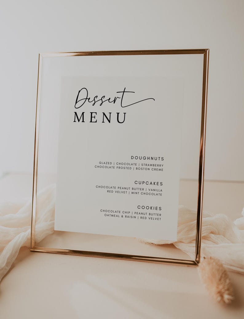 May include: A gold-framed menu board with a white background and black text. The menu lists dessert options, including doughnuts, cupcakes, and cookies. The text reads: "Dessert Menu", "Doughnuts", "Glazed | Chocolate | Strawberry", "Chocolate Frosted | Boston Creme", "Cupcakes", "Chocolate Peanut Butter | Vanilla", "Red Velvet | Mint Chocolate", "Cookies", "Chocolate Chip | Peanut Butter", "Oatmeal & Raisin | Red Velvet".