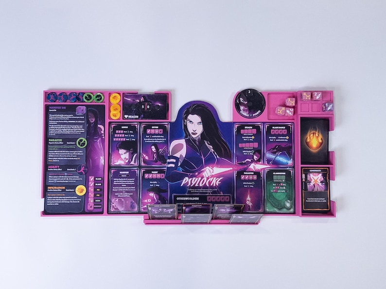 May include: A pink plastic board game organizer for Psylocke featuring dedicated slots for character cards, tokens, and dice. The center displays a large illustration of the character Psylocke with purple and black accents, alongside various game components and text labels.