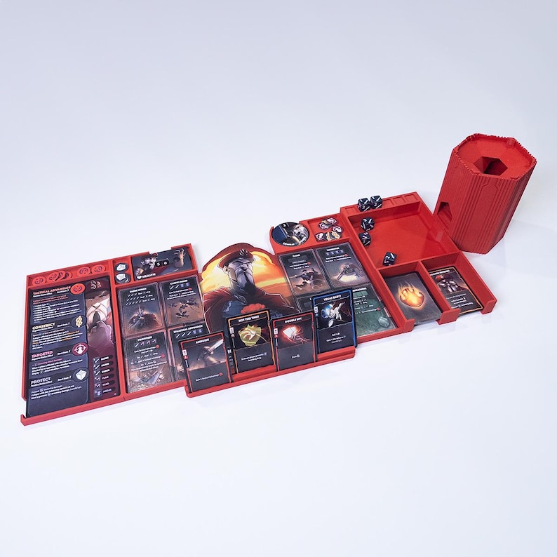 May include: A red plastic board game organizer tray set featuring multiple compartments for cards, tokens, and dice. The set includes a tall hexagonal dice tower, various slots for game cards, and dedicated spaces for small circular tokens and game pieces.
