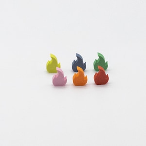 May include: Six small, three-dimensional flame-shaped tokens in a variety of matte colors including lime green, light blue, forest green, light pink, orange, and red. Each token features a pointed, stylized fire design with a flat base.