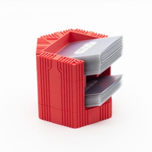 May include: A red, hexagonal card holder with two tiers, each holding a stack of cards. The cards have a gray and white design with the word "STAR WARS" visible. The holder has a textured, ribbed design and is made of plastic.