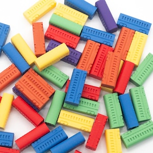 May include: A collection of small, rectangular wooden game pieces in various colors including red, blue, yellow, green, orange, and purple. Each piece features a series of small, etched vertical lines along one side, resembling a train car.