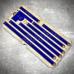 May include: A wooden ruler with blue markings and the text "GAMING FORGE". The ruler has several parallel blue lines and markings for inches. The design includes a blue "G" logo and the text "GAMING FORGE".